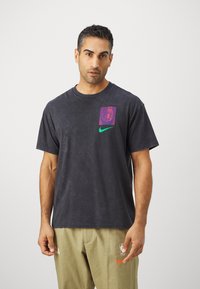 Men's dark gray cotton t-shirt featuring a purple graphic on the left chest and a green Nike logo accent. Short sleeves, relaxed fit.