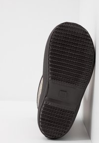 Suela de zapato de goma negra con patrón de textura en la suela. Logotipo circular y la impresión del tamaño 28 son visibles en la zona del talón. Se encuentra contra un fondo blanco.
