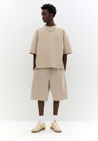 Pulover bej oversize cu mânecă scurtă și pantaloni scurți asortați, fabricate dintr-un material moale; asortat cu încălțăminte bej cu accente galbene și șosete albe.