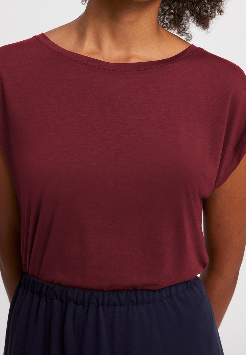 Burgundské triko s krátkým rukávem z lehkého materiálu, s širokým výstřihem a volným střihem, doplněné tmavě navy elastickým páskem.