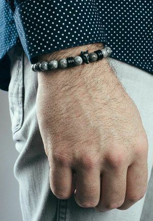 Black and gray bead bracelet featuring a textured star accent, worn on a wrist with light skin, against a dotted shirt.