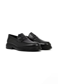 Mocasines de cuero negro con un acabado suave, que cuentan con un detalle de costura elevada y suelas de goma flexibles. Diseño clásico adecuado para ocasiones formales.