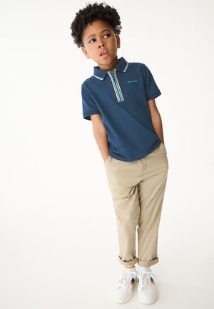Mörkblå polo skjorta med en färgglad randig knappslå, ihopparad med beige byxor och vita sneakers med flerfärgade detaljer.