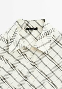 Chemise blanche à boutons avec un motif à carreaux noir et beige et un col, étiquetée Massimo Dutti, fabriquée au Portugal.
