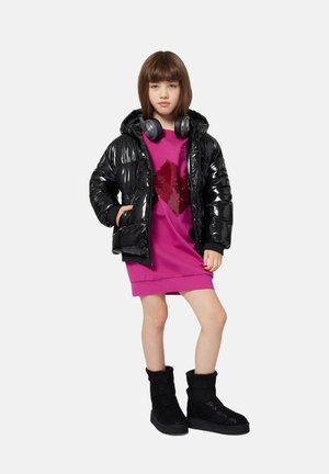 Doudoune noire, texture brillante, portée sur un sweat-shirt rose avec un design de cœur en sequins. Associée à des bottes en fourrure noires et des écouteurs.