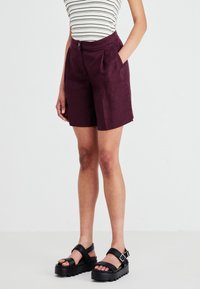 Bordeaux linshorts med en skreddersydd design, folder og sidelommer, parret med svarte kraftige sandaler med justerbare stropper.