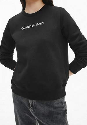 Schwarzes Sweatshirt mit langen Ärmeln und rundem Ausschnitt. Mit weißem "CALVIN KLEIN JEANS"-Logo auf der Vorderseite. Weiche Stofftextur.
