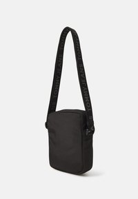Borsa a tracolla nera realizzata in tessuto con forma rettangolare. Presenta una chiusura con zip e una tracolla regolabile con il marchio "TOMMY JEANS".