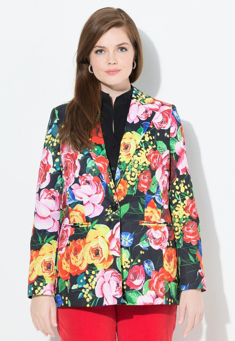 Svart blommig kavaj med livfulla ros- och bladmönster, slag och två framfickor. Bärs över en svart topp och röda byxor.