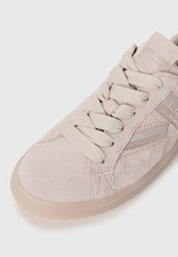 Baskets en suede beige clair avec un bout rond, lacets en tissu, texture subtile et semelle en caoutchouc. Présente une marque discrète sur le côté.