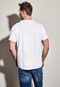 Bílý bavlněný tričko s krátkými rukávy a kulatým výstřihem, v kombinaci s modrými džínami. Hladká textura a volný střih.