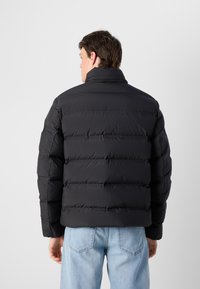 Zwarte pufferjas met een doorgestikt ontwerp. Hoge kraag en ribgebreide manchetten. Gecombineerd met lichtblauwe, comfortabele jeans. Effen, matte afwerking.