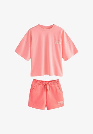 Laza, rövid ujjú rózsaszín póló és hozzáillő, zsinóros rövidnadrág szett, mindkettőn "Baker Girls Club" felirat a mellkason és a lábszáron.