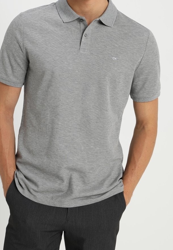 Polo gris en mélange de coton ; manches courtes, col classique et petit logo sur la poitrine. Associé à un pantalon foncé.