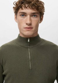 Jersey con cuello de cremallera en verde oliva, textura acanalada, con un cuello alto y cremallera corta, que enfatiza un diseño ajustado.