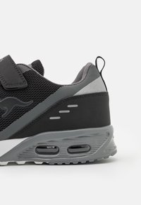 Schwarzer Sportschuh mit Obermaterial aus Mesh, synthetischen Akzenten und grauen Details. Verfügt über einen Klettverschluss, Luftpolsterung und eine strukturierte Sohle.