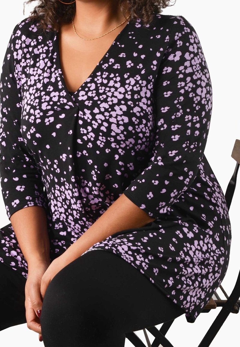 Černá tunika s výstřihem do V a třičtvrtinovými rukávy, zdobená fialovými skvrnami. Nalezena na osobě sedící na židli, oblečená přes černé leginy.