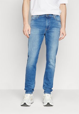 Jeans in denim azzurro chiaro con un taglio slim. Presentano un classico design a cinque tasche e una leggera sfumatura. Abbinati a scarpe da ginnastica bianche.