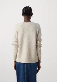 Bežna volnena pulover s dolgimi rokavi, raglan krojem, okroglo izrezano ovratnikom in rebrastimi manšetami, nošen čez modro jeans krilo.