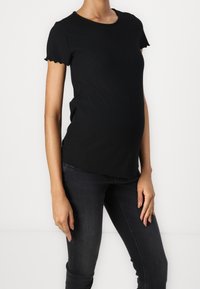 Black ribbed t-shirt with short scalloped sleeves, a round neckline, and a slightly curved hem, paired with dark denim jeans.