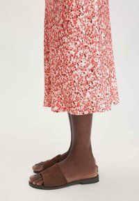 Braune Wildleder-Sandalen mit einem breiten Riemen, kombiniert mit einem knieumspielenden, rosa Kleid mit Blumenmuster, das eine weiche, fließende Textur und ein halbtransparentes Finish aufweist.