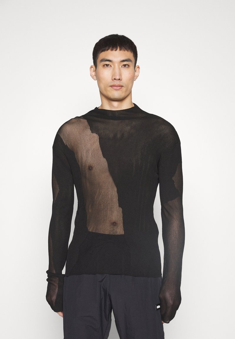 Maglia nera a maniche lunghe in maglia con un torso trasparente e una texture rigata solida sulle maniche e sul collo. Sezioni ritagliate evidenziano la pelle.
