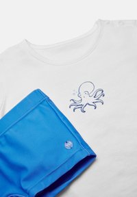 Camisa blanca de manga corta con un gráfico de pulpo, combinada con pantalones cortos de baño azules que presentan un acento de logo circular en el dobladillo.