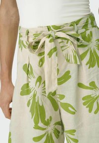 Světle béžové látkové kalhoty s velkým zeleným květinovým vzorem, zavazovacím páskem v pase a záhyby pro zdůraznění detailů.