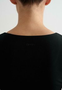 Indumento nero con scollatura ampia e arrotondata, design aderente e texture liscia, che mostra la zona del collo sul retro. Branding sottile visibile.