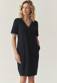 Robe bleu marine au design en V, à manches courtes avec des finitions blanches, dotée de deux poches avant et d'une coupe droite avec des fentes sur les côtés.