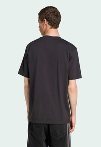 Sort bomulds t-shirt med kortærmer og rund halsudskæring, med en ensfarvet ryg og en afslappet pasform. Blandet med mørke denim-bukser.