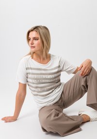 White T-shirt with horizontal beige stripes featuring textured patterns. Smooth fabric, relaxed fit. Paired with beige wide-leg pants and white sneakers.