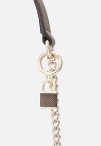 Brunt tekstureret rem med guldfarvet beslag, der har en kæde og en lille hængelåsdetaile. Designet lægger vægt på en blanding af materialer og finish.