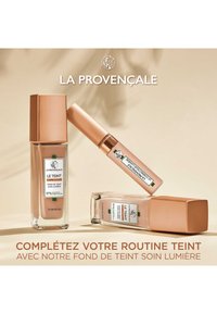 Bouteilles de fond de teint de différentes formes : un design carré et un design rectangulaire en verre transparent avec des bouchons en or rose. Étiquettes visibles sur chacune.