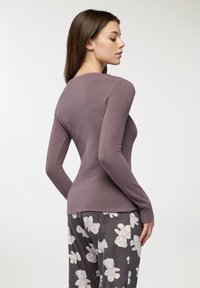 Długi rękaw w stonowanej mauwowej tkaninie, dopasowany krój z okrągłym dekoltem. Noszony z szarymi spodniami w print niedźwiadka.