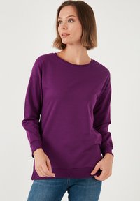 Felpa viola a maniche lunghe con scollatura e polsini a coste, caratterizzata da un fondo dritto e una texture di tessuto morbido e liscio.