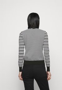 Striped sweater in black and white, featuring a fitted design with a green ribbed hem and cuffs. Smooth texture, long sleeves.