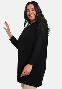 Black long-sleeve tunic sweater with textured knit, featuring studded accents on the shoulders, relaxed fit, and ribbed cuffs.
