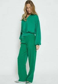 Top verde, morbido e largo con scollo a V e maniche lunghe abbinato a pantaloni larghi coordinati. Tessuto morbido con una superficie liscia.