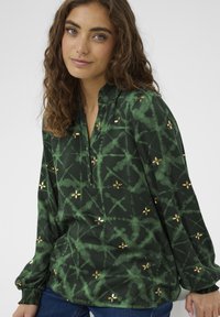 Green, patterned blouse in soft fabric features gold floral accents, a v-neckline, and gathered cuffs. Ideal for casual wear.