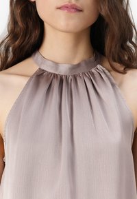 Satin-Haltertop in hellem Mauve mit plissiertem Ausschnitt. Glatte Textur und minimale Details, die eine lockere Passform um die Schultern schaffen.