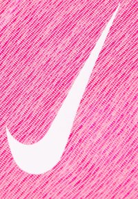 Logo de swoosh blanco de Nike sobre un fondo de tela texturizada rosa, primer plano que muestra los detalles del tejido.