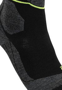 Svart och grå strumpa med vadderad häl och fotvalvsstöd. Har en klar gul accent upptill och strukturerade områden för grepp.