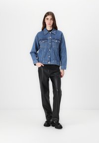 Denim jakna svetlo modre barve z gumbi spredaj, dvema žepoma na prsih in sproščenim krojem. V kombinaciji z elegantnimi črnimi hlačami iz umetnega usnja.