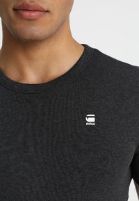 Černá bavlněná tričko s kulatým výstřihem. Na hrudi je malá bílá loga "RAW". Měkká textilie a přiléhavý střih.