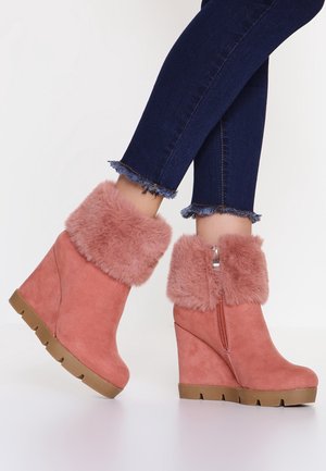 Bottines roses à talons compensés avec semelles épaisses marron et manches en fourrure douce, portées avec un jean skinny foncé à ourlet effiloché.