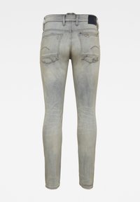 Jeans de mezclilla azul claro deslavado con corte ajustado, que cuentan con un yugo trasero, dos bolsillos traseros de parche y un desgaste mínimo.