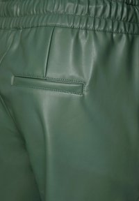 Vihreät nahkahousut, joissa on sileä pinta ja joustava vyötärönauha. Sisältää pystysuoran takataskun, jossa on ommeltu yksityiskohta.