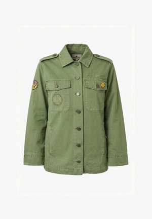 Giacca verde in stile militare con chiusura a bottoni, tasche sul petto, patch con il simbolo della pace, spilla con faccina sorridente e toppa ricamata con la scritta "Stay Weird".