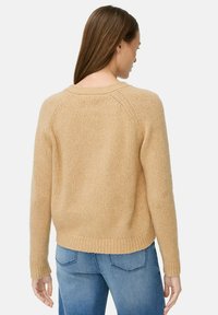 Beige gestrickter Pullover mit weitem Halsausschnitt und gerippten Bündchen. Der Rücken hat Raglanärmel und einen lockeren Schnitt, kombiniert mit Jeans.